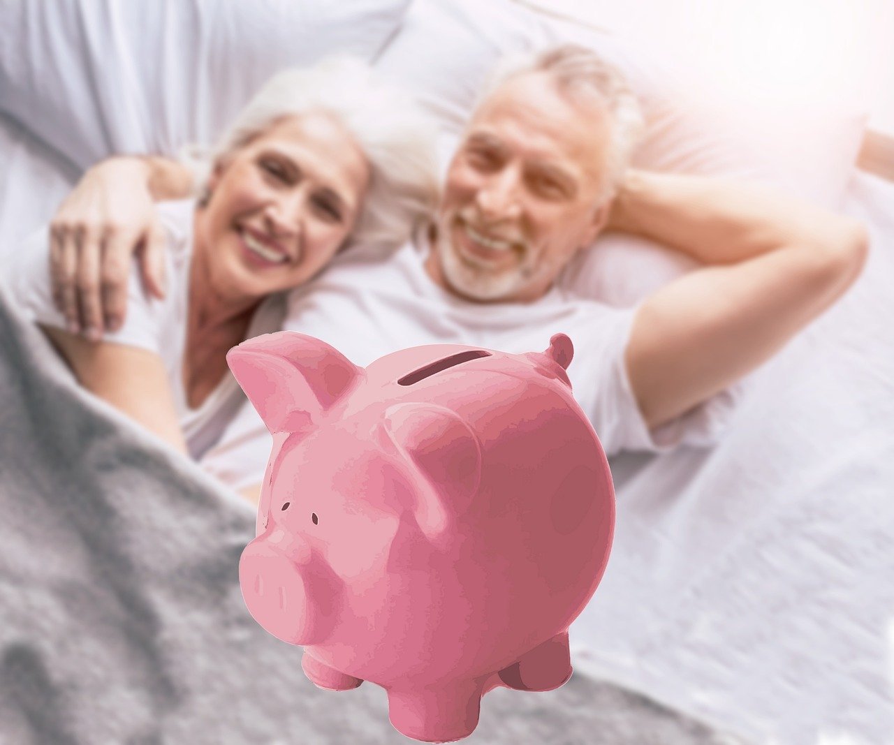 smiling retirees relaxing in bed with a pink piggy bank in the foreground representing their nest egg