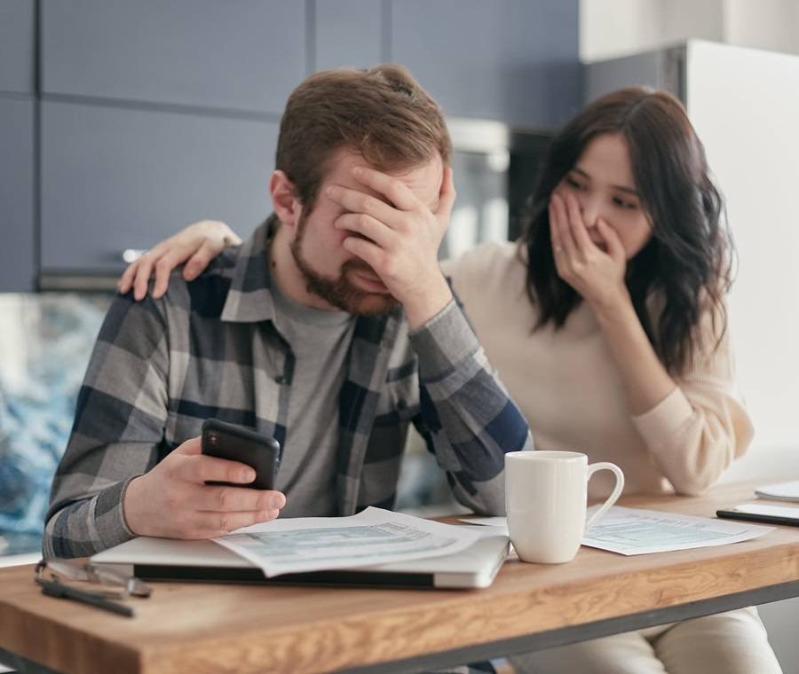 man covering his face in frustration checking expenses and debts with partner comforting him
